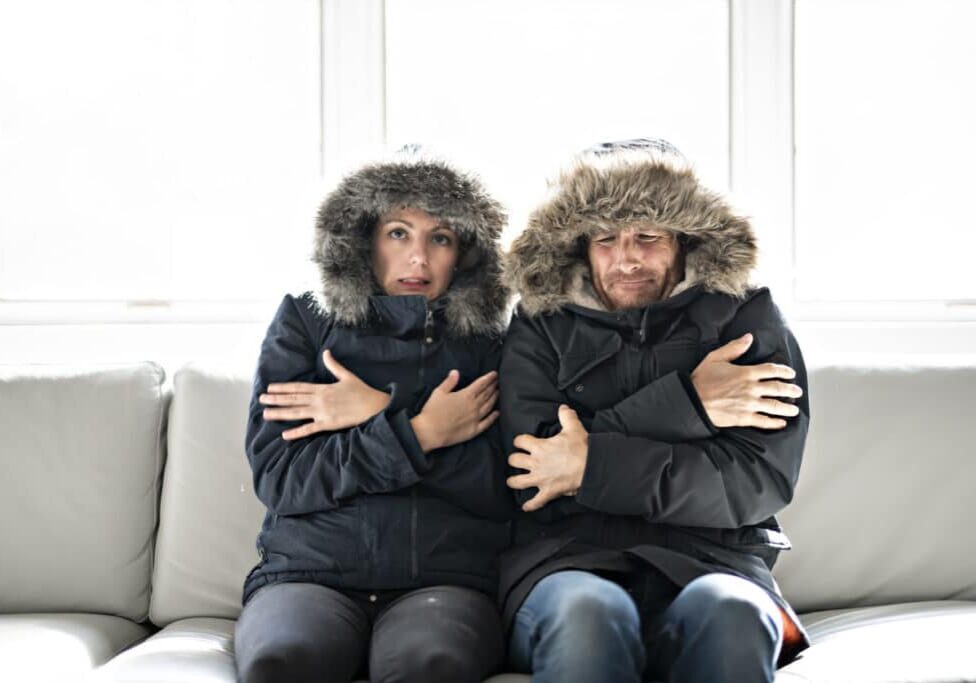 Couple have cold on the sofa at home with winter coat A couple have cold on the sofa at home with winter coat